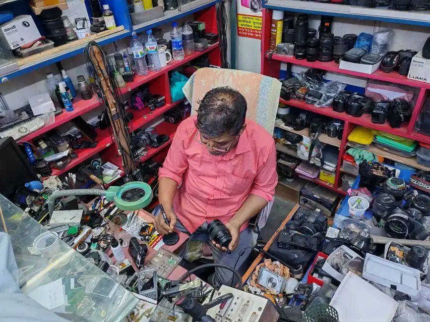 A camera technician in a workshop examining and repairing a camera lens amidst various tools and equipment.