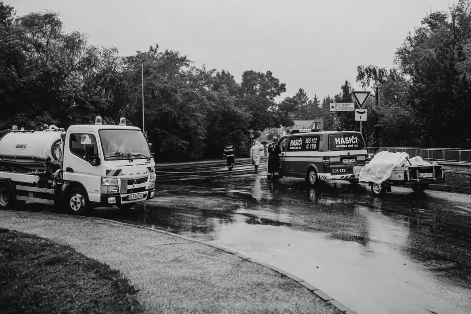 Black and white image of emergency vehicles on a rainy street with first responders.