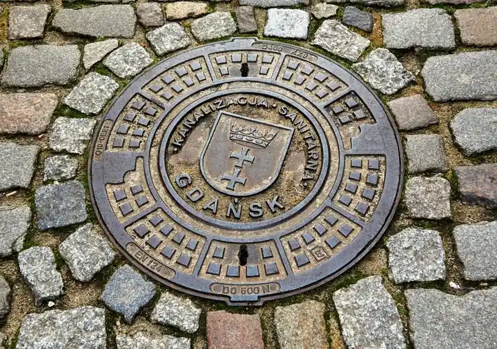 Circular Gdańsk manhole cover set in cobblestone street, showcasing urban infrastructure.